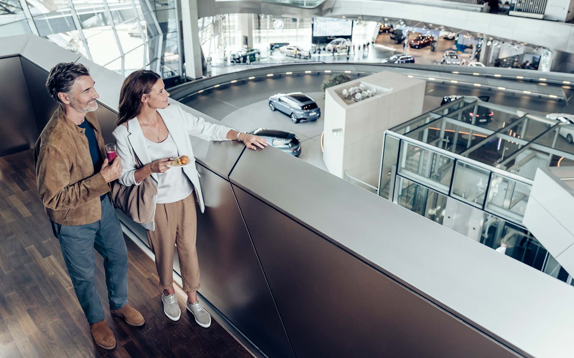 Glückliches Paar geniesst den Ausblick von der Galerie auf die zur Abholungbereitgestellten Fahrzeuge in der BMW Welt