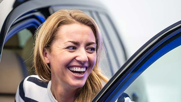 Frau steigt lächelnd in ihren neuen BMW bei der Auto Abholung in der BMW Welt