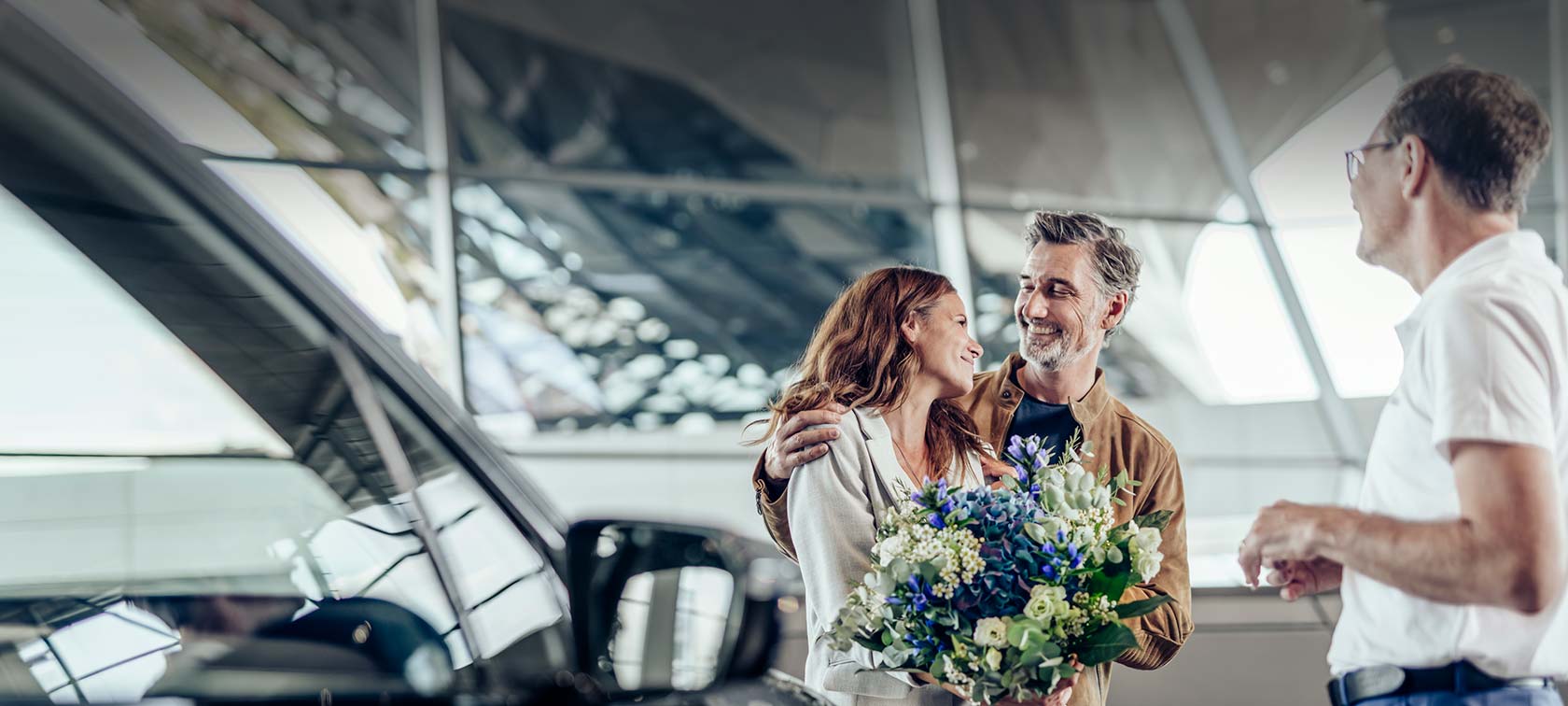 Glückliches Paar bei der Fahrzeugübergabe in der BMW Welt mit Berater und Blumenstrauss