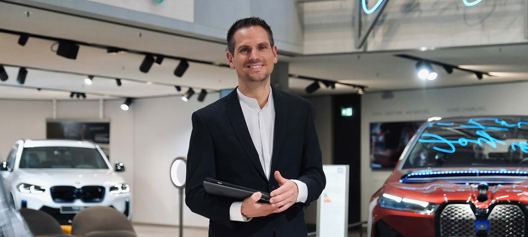 Smiling man in suit holds tablet for vehicle consultation at BMW Welt.