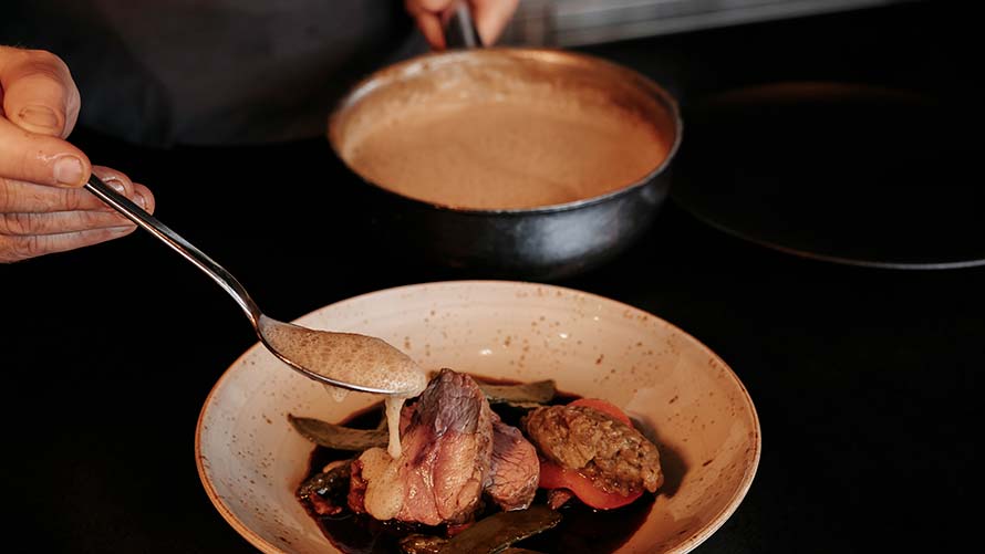 chef pours sauce on fine beef dish chef pours sauce on fine beef dish