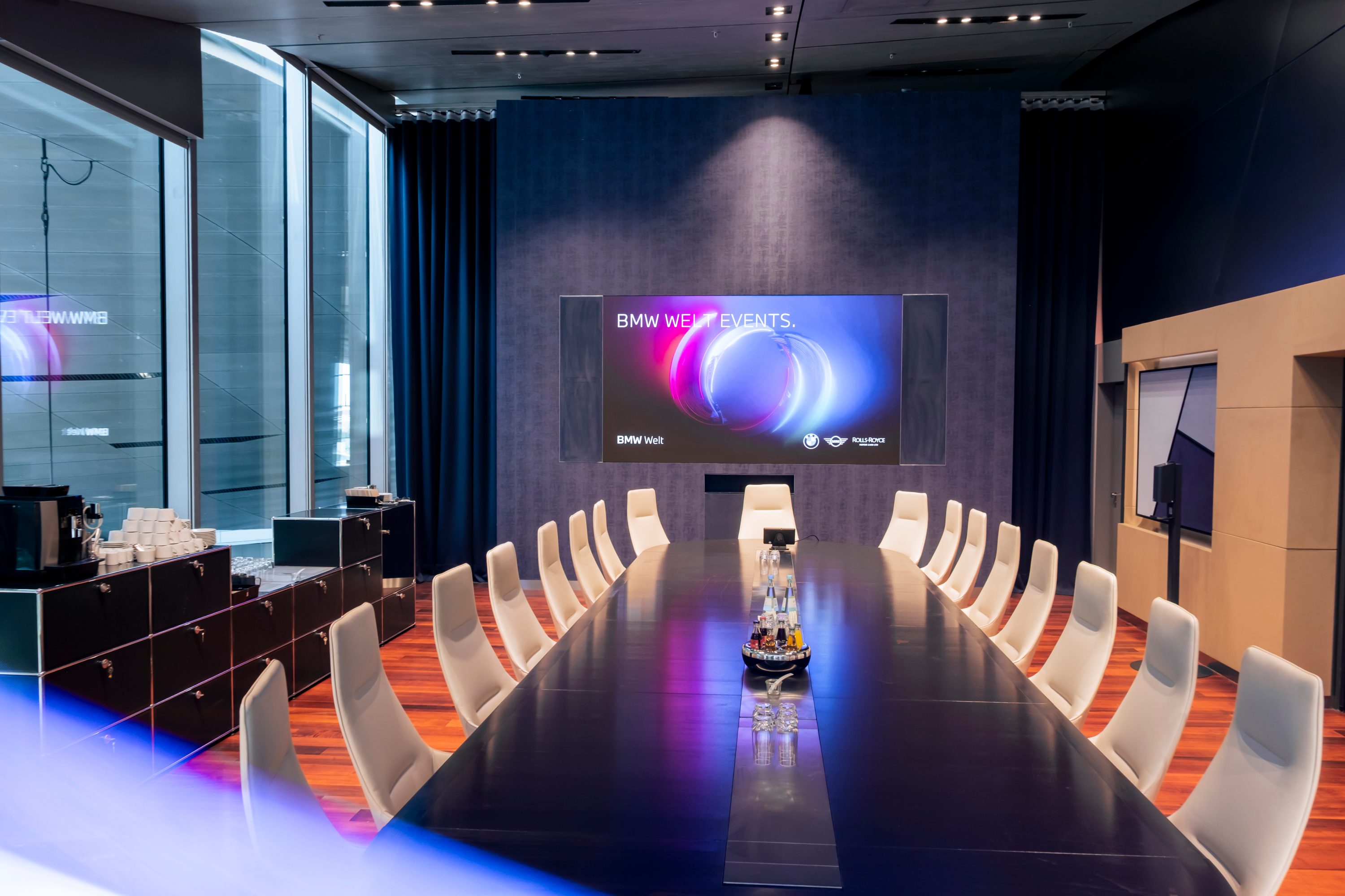 View into conference room with large table and white seating in Business Club of BMW Welt
